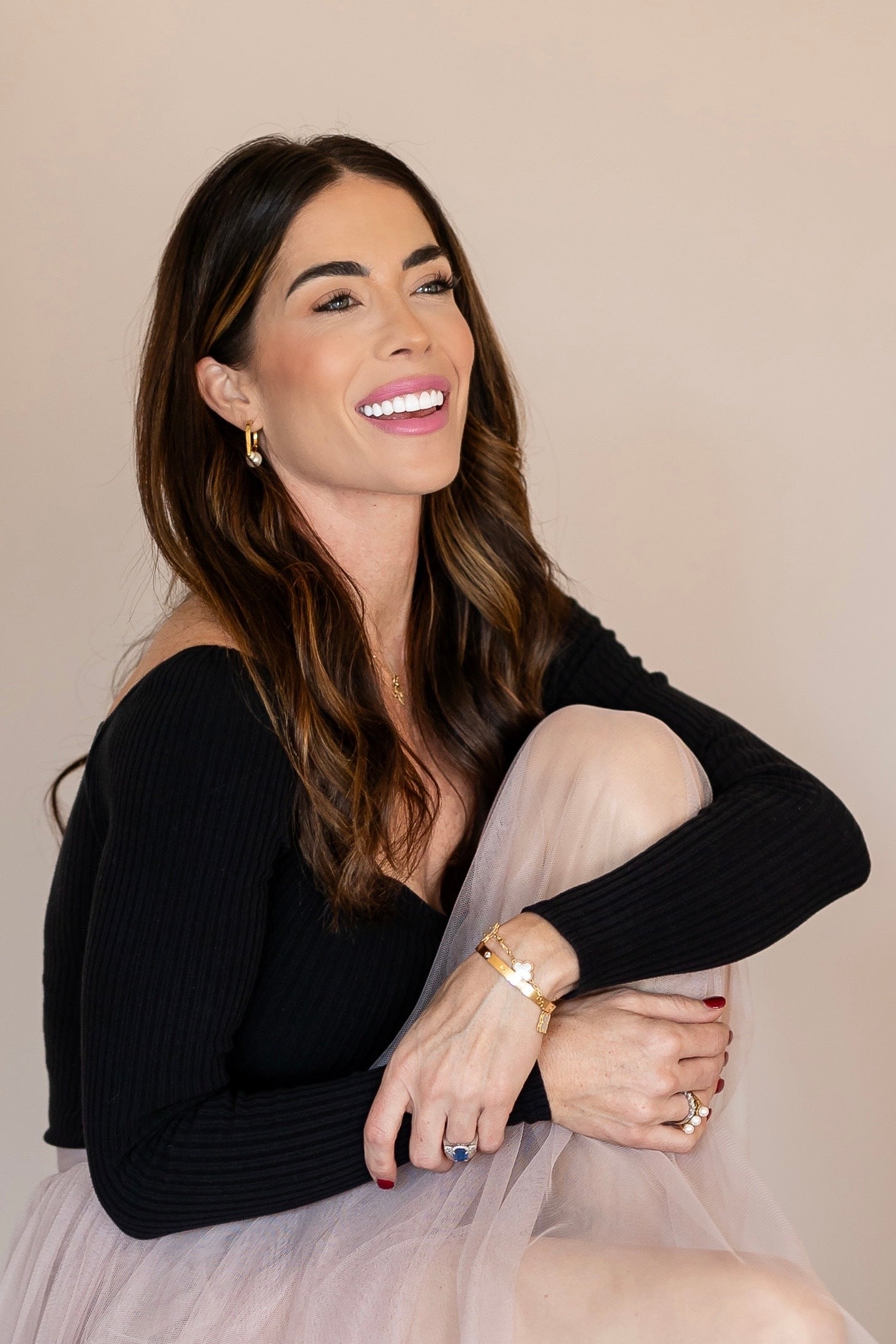 Woman wearing a black top and light pink skirt with jewelry on a beige background