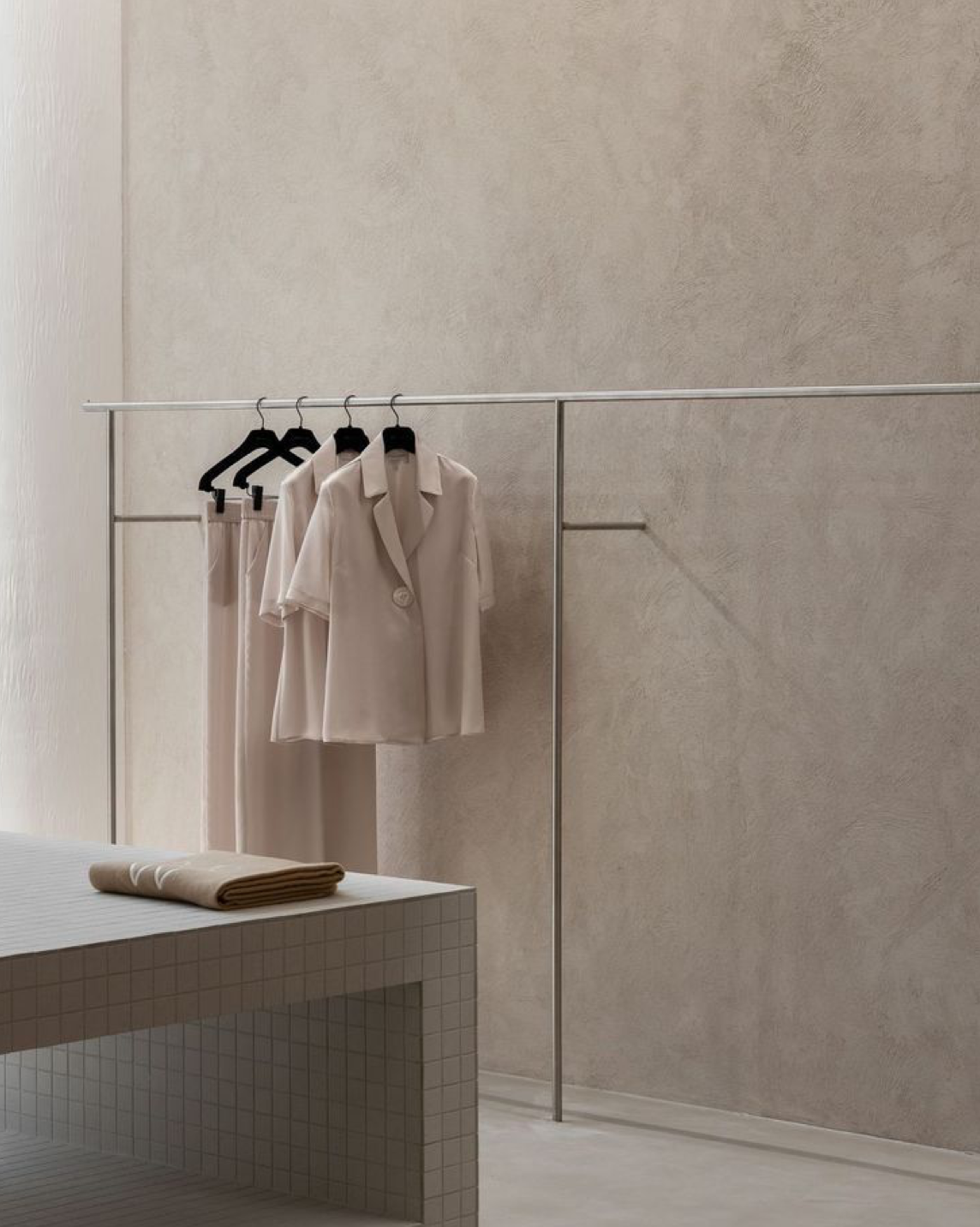Beige clothing on a rack against a neutral wall with a tiled bench.